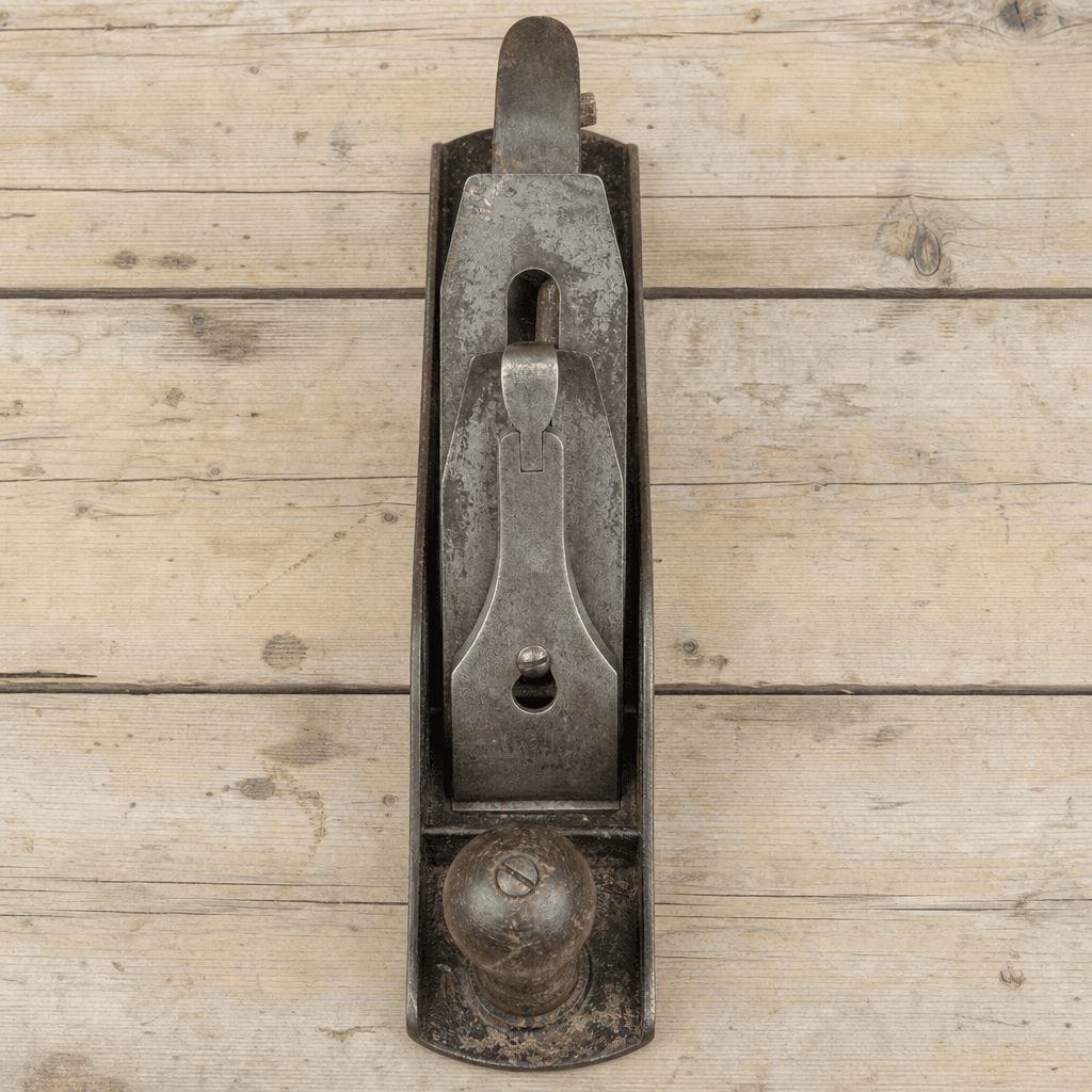 A worn steel hand plane with a wooden knob, photographed straight on, on bare pine boards.